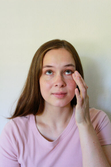 A young woman applies concealer to the under-eye area of her face. Getting Started With Makeup