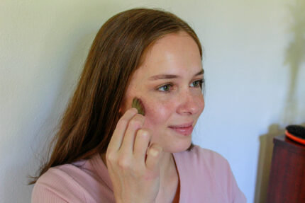 A young woman applies blush to her cheeks with a makeup brush. Getting Started With Makeup
